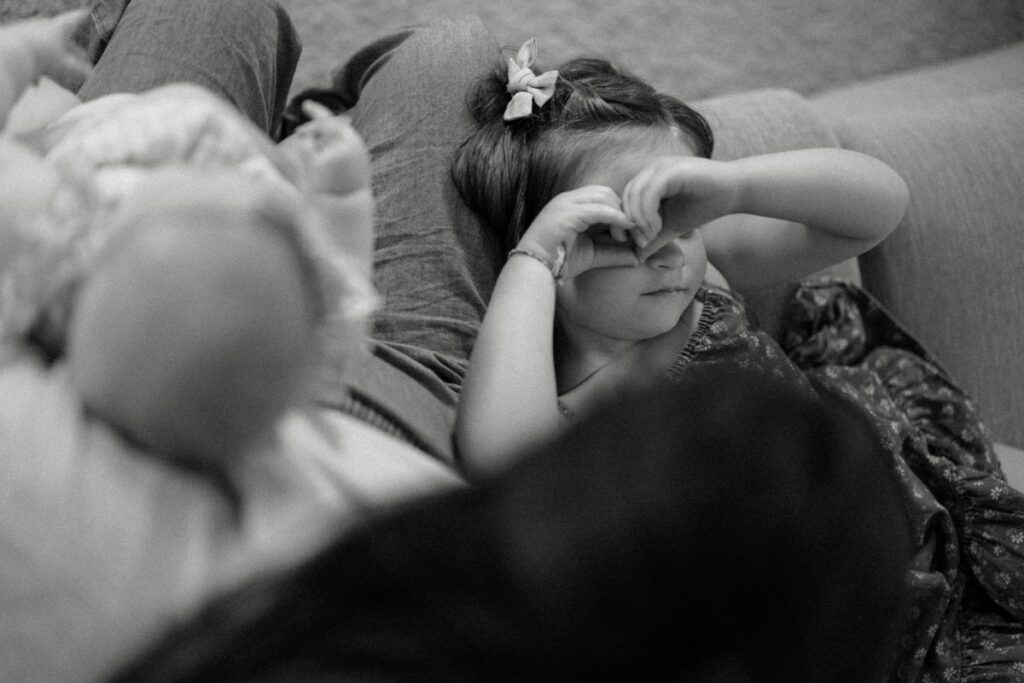 a daughter sitting on the couch with her mama while looking at her through a heart shape she made with her hands