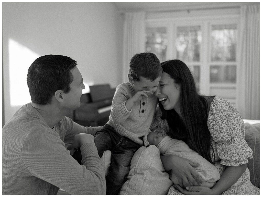 mom and son share a joyful moment of laughter while mama holds her new baby girl