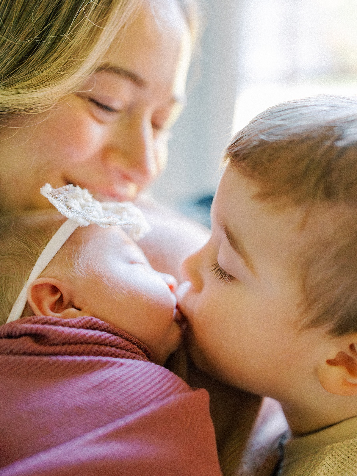 a mother glances down at her son as he kisses his new sister